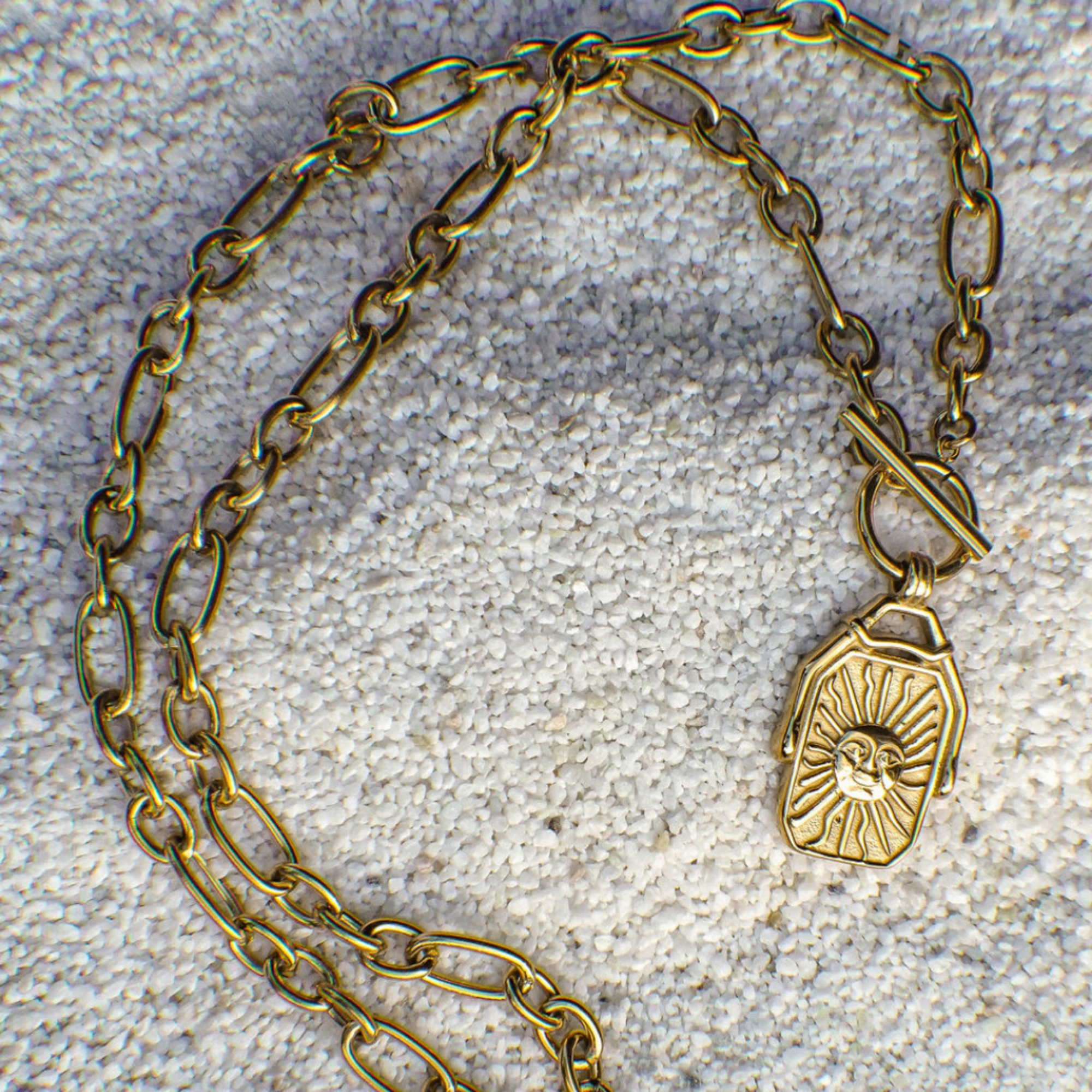 Gold chain bracelet with a pendant on a textured surface
