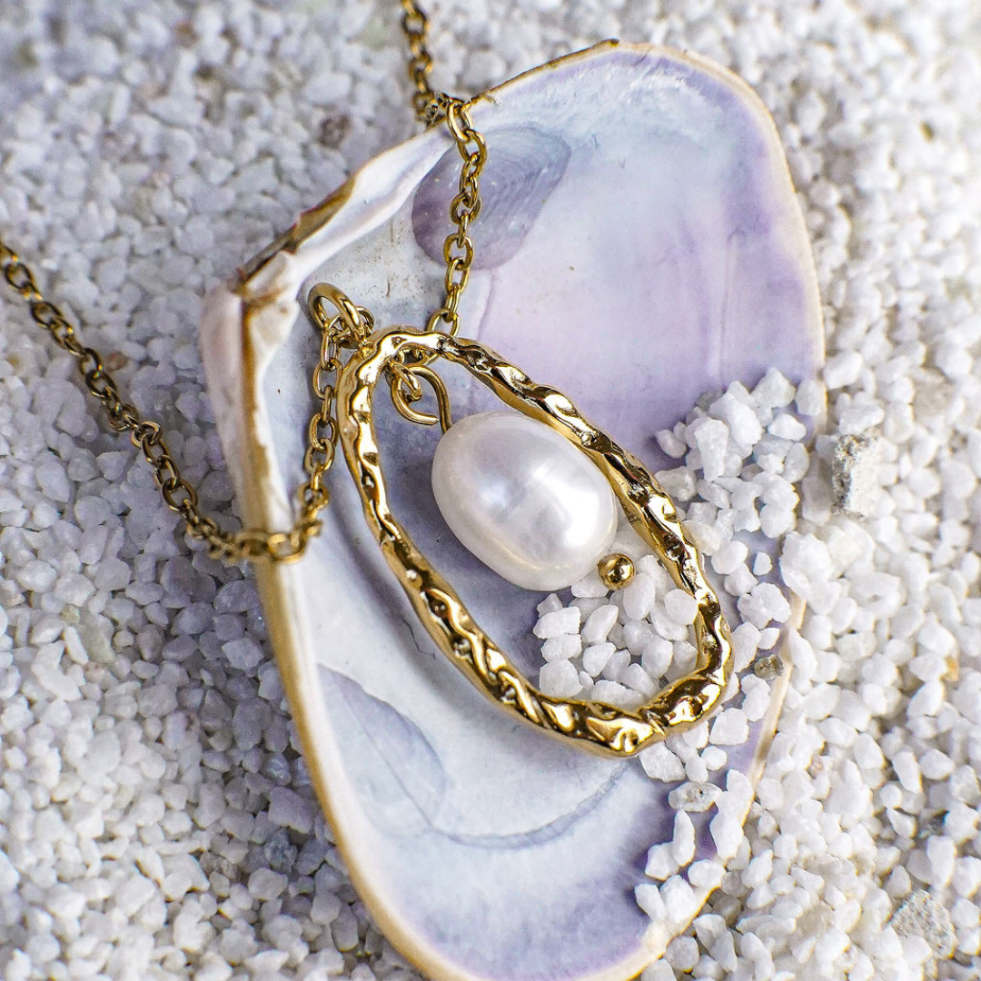 Gold necklace with a pearl pendant on a textured surface