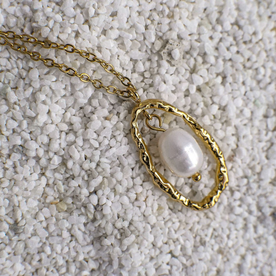 Gold necklace with a pearl pendant on a textured white surface