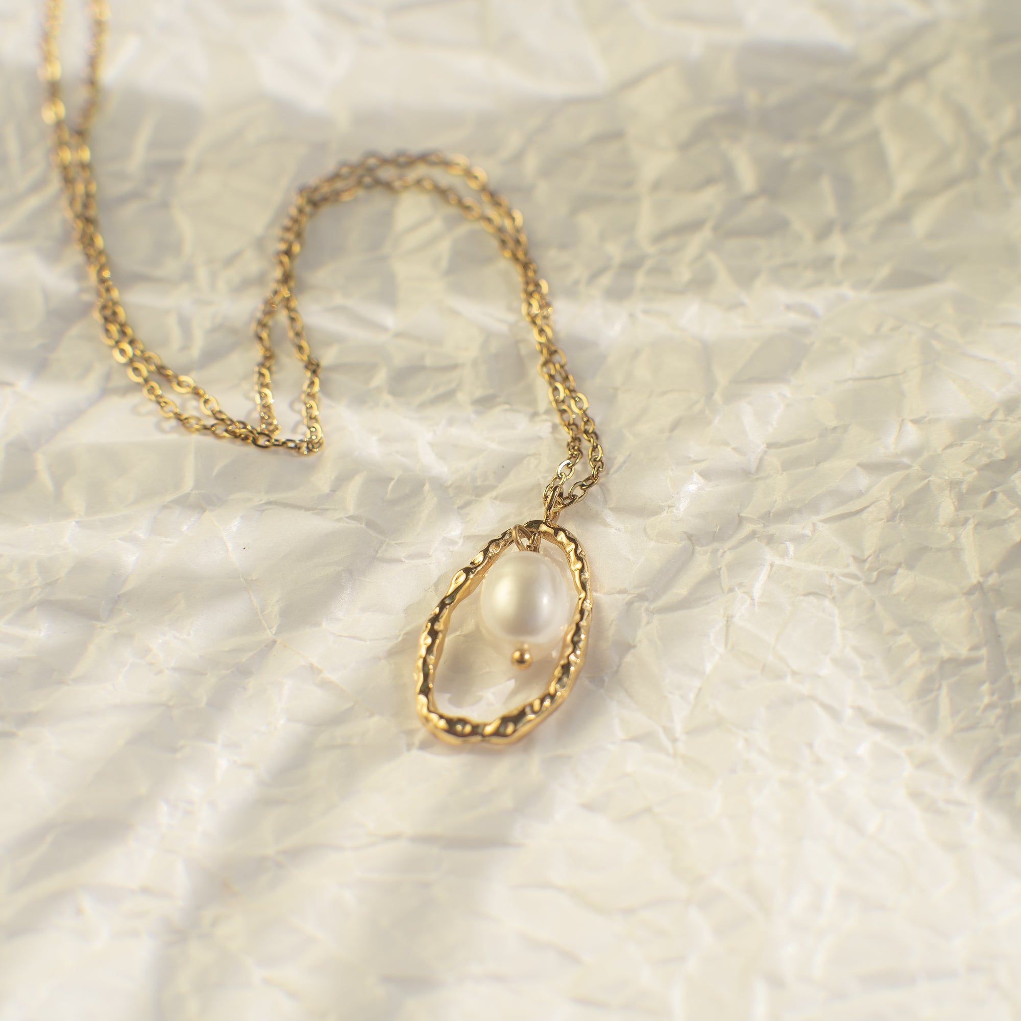 Gold necklace with a pendant on a textured beige background
