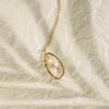 Gold necklace with a teardrop-shaped pendant on a textured beige background