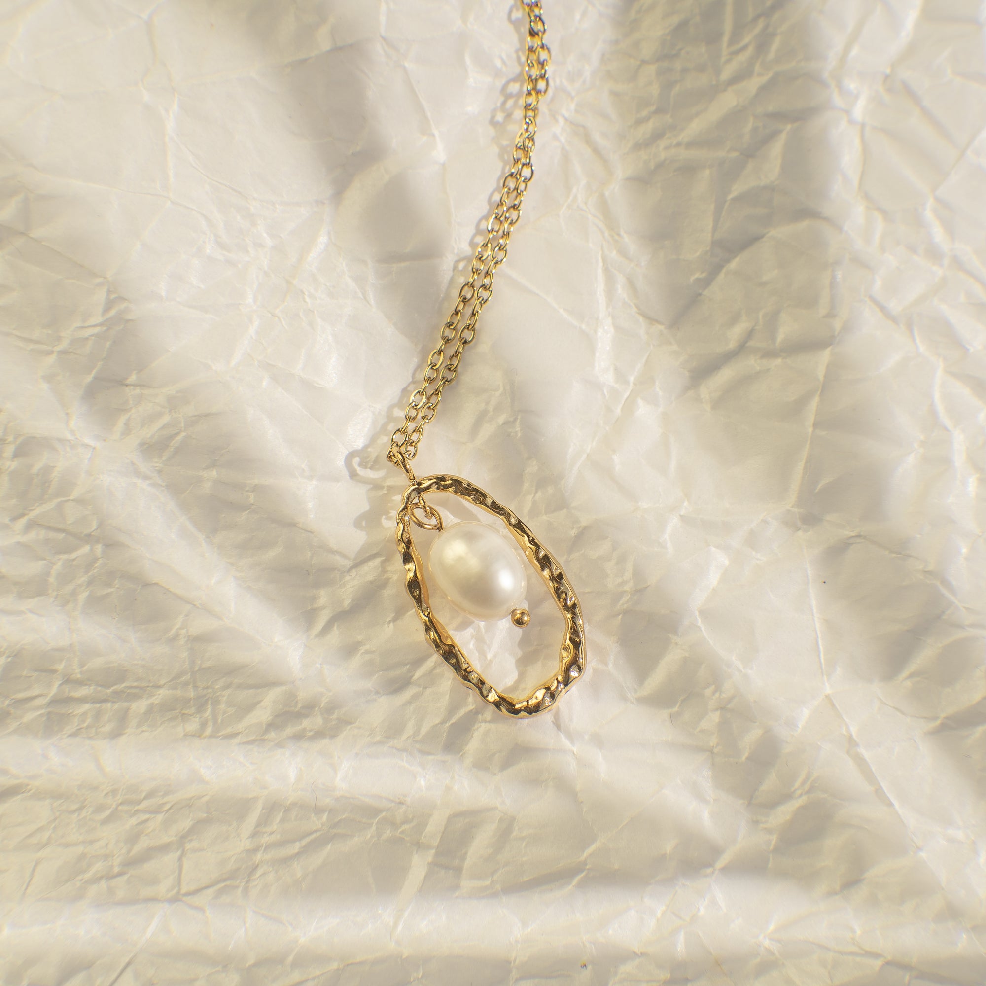 Gold necklace with a teardrop-shaped pendant on a textured beige background