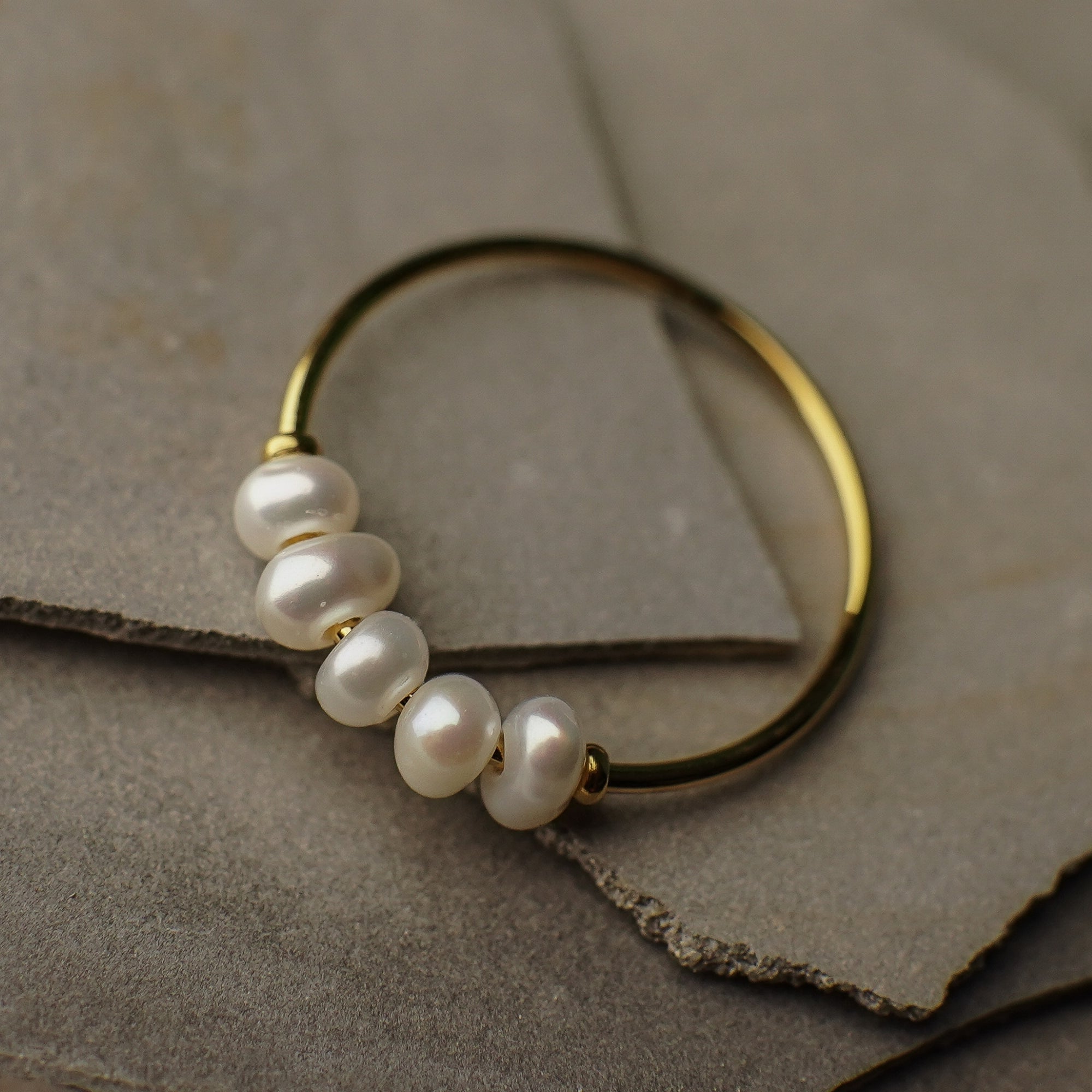 Gold hoop earring with pearls on a textured surface