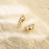 Pair of gold earrings with clear gemstones on a beige textured background