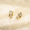 Gold earrings with clear gemstones on a soft beige background