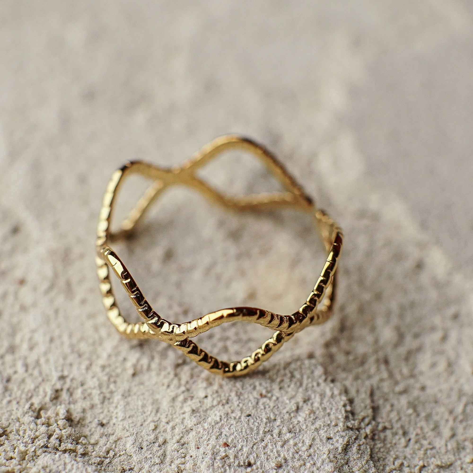 Gold ring with a textured design on a sandy background