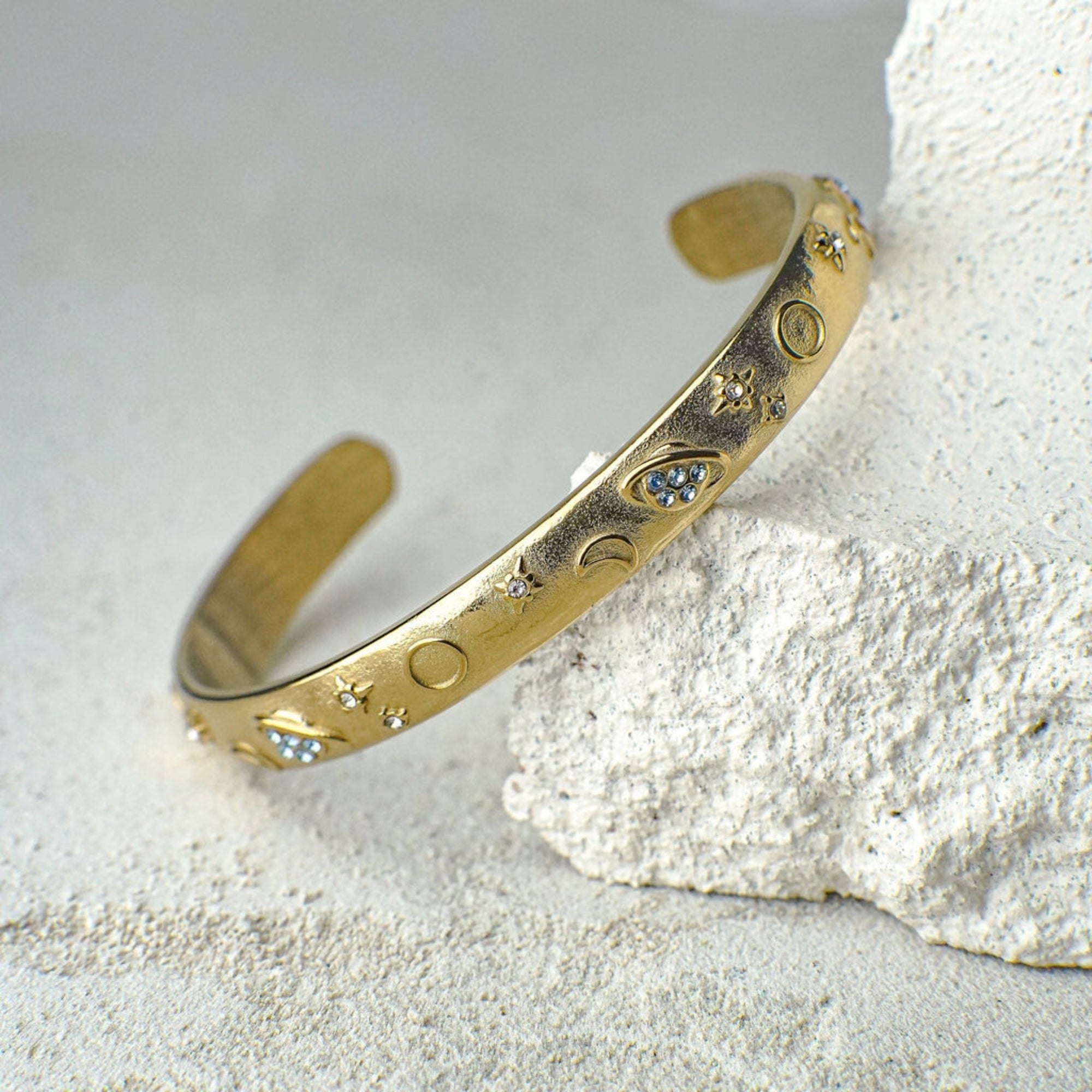 Gold bracelet with celestial design on a textured surface