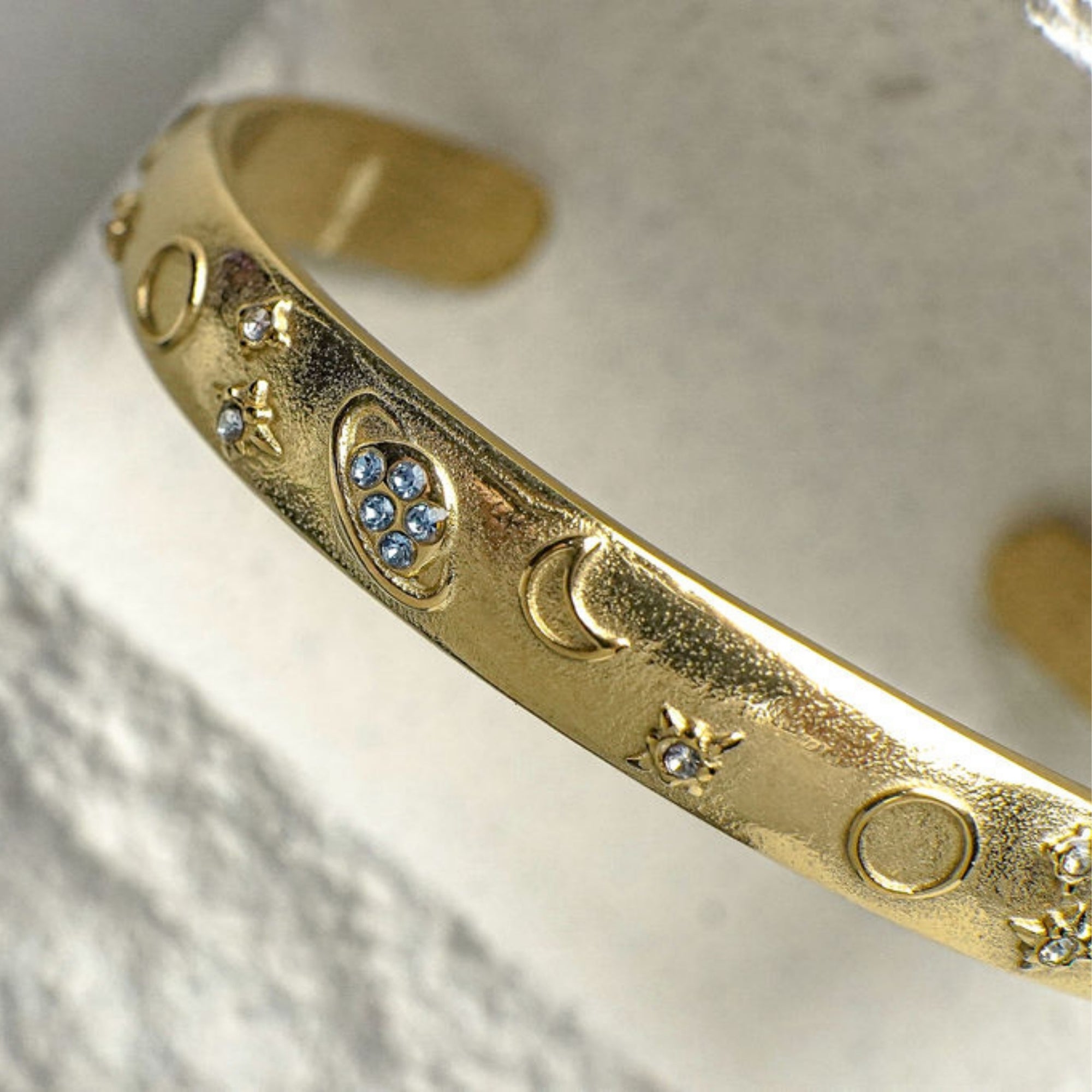 Gold bracelet with celestial designs on a textured surface
