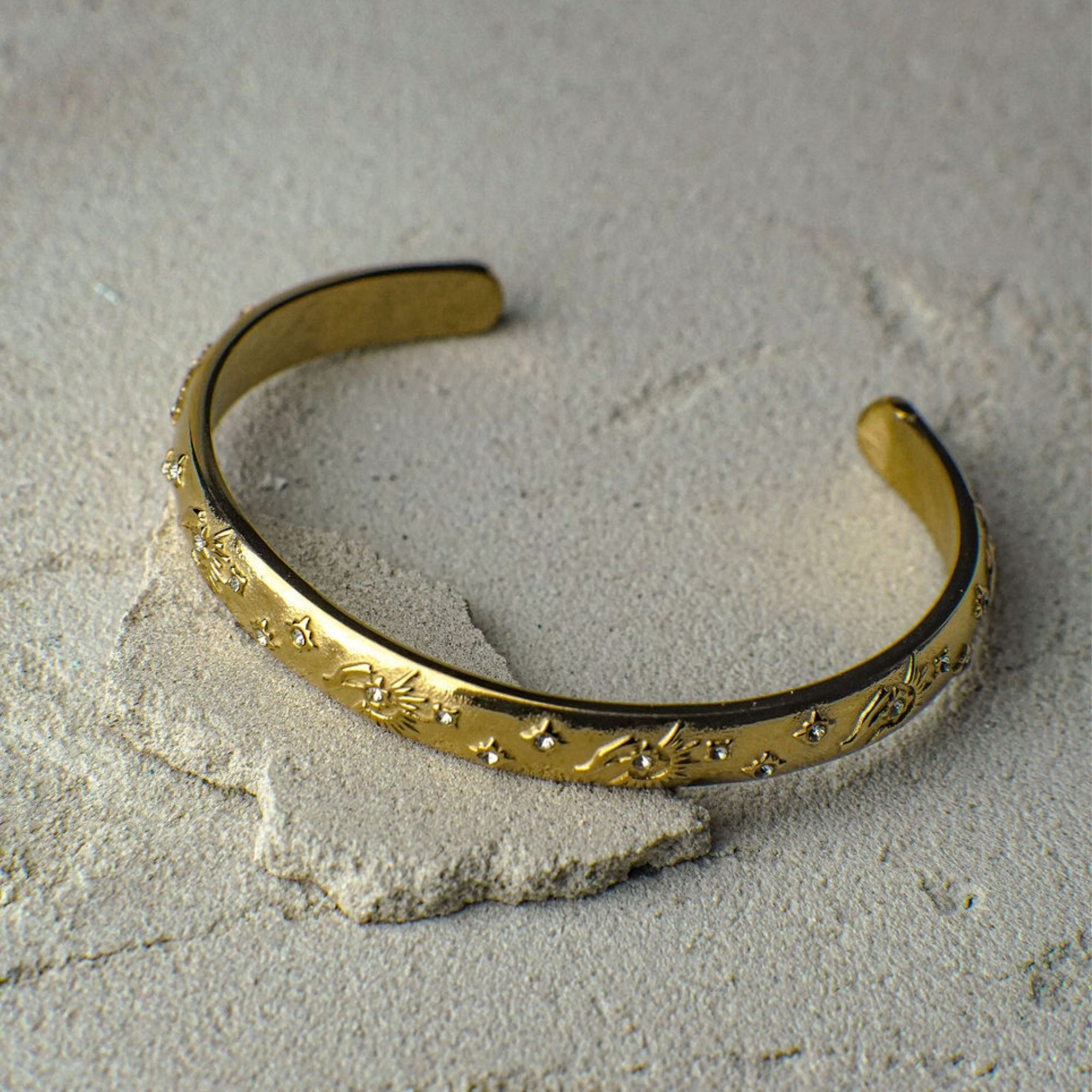 Gold bracelet with intricate designs on a textured beige surface