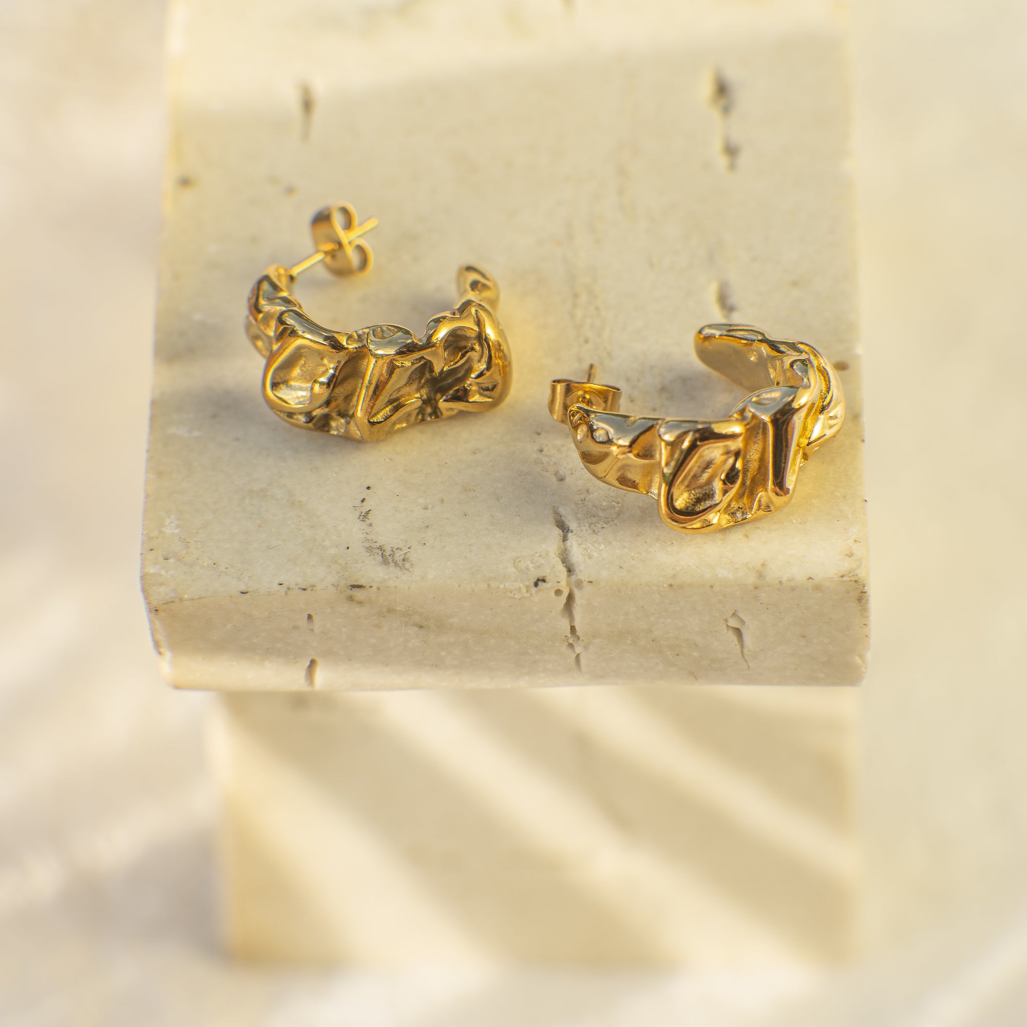 Gold hoop earrings on a textured beige surface