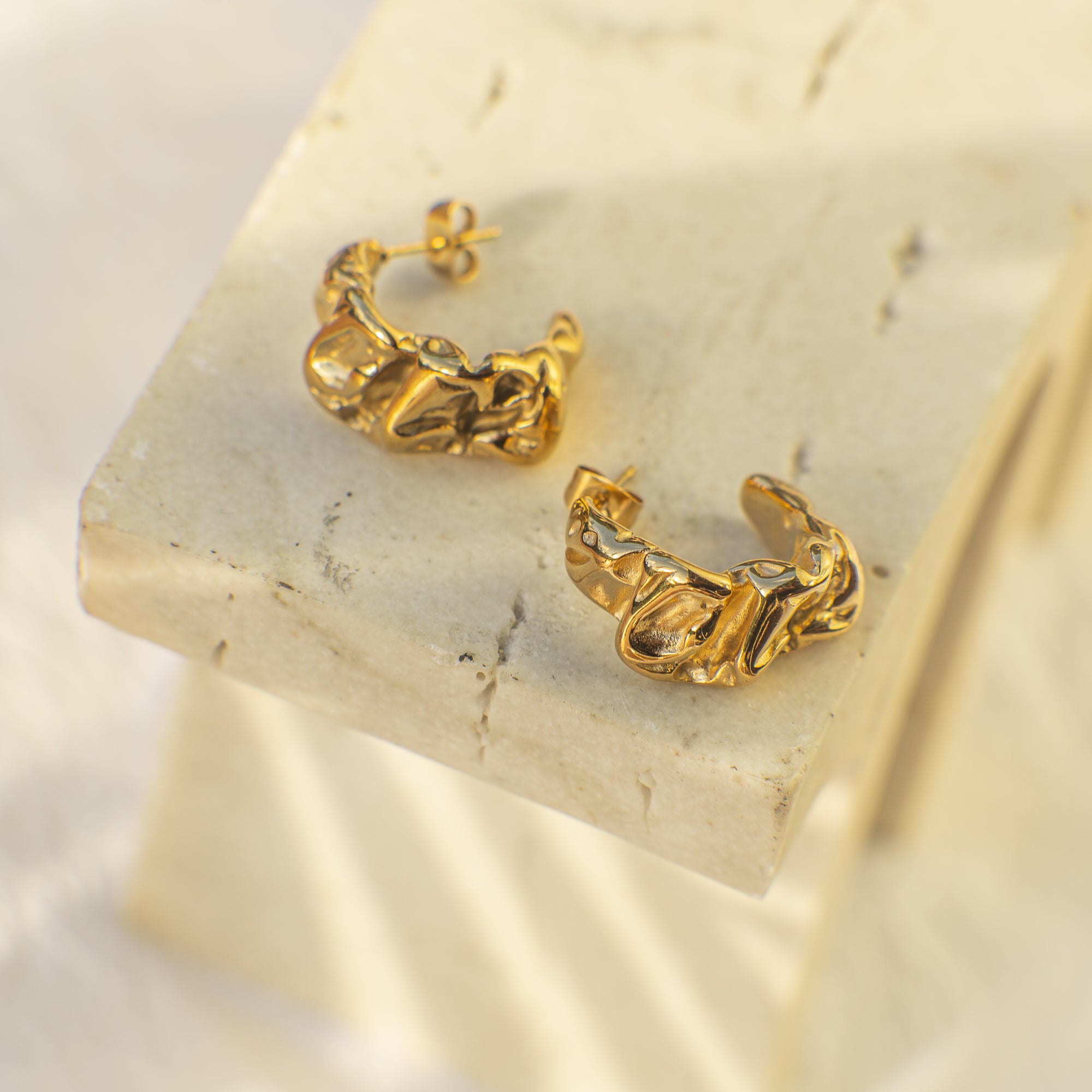 Gold hoop earrings on a light stone surface