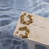A pair of gold abstract earrings on a beige wooden surface