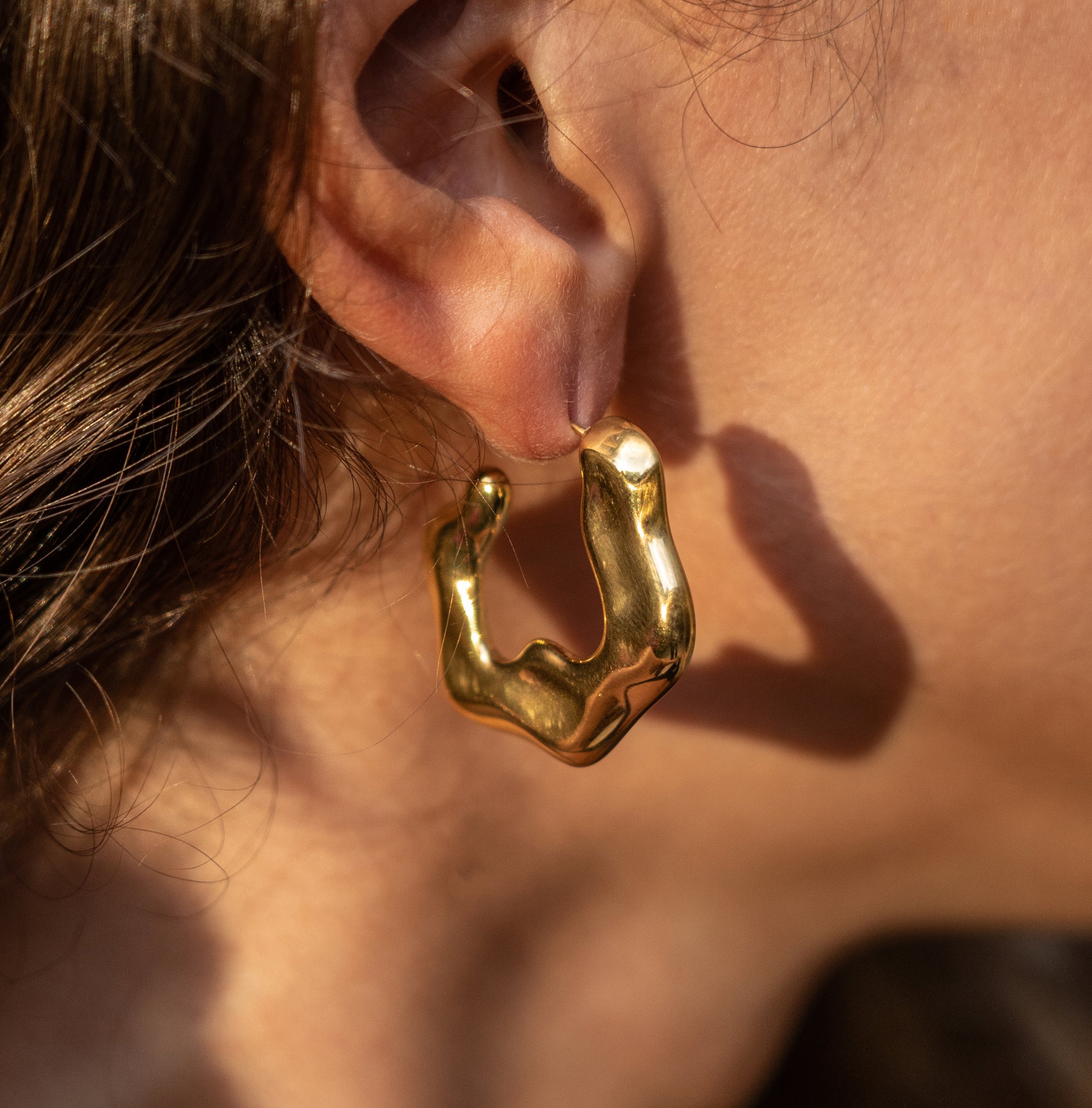 An gold abstract earring on a model's ear