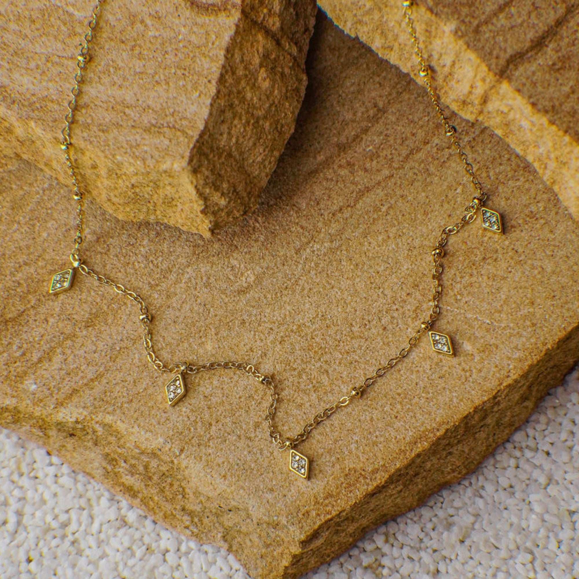 Gold necklace with diamond-shaped pendants on a stone surface