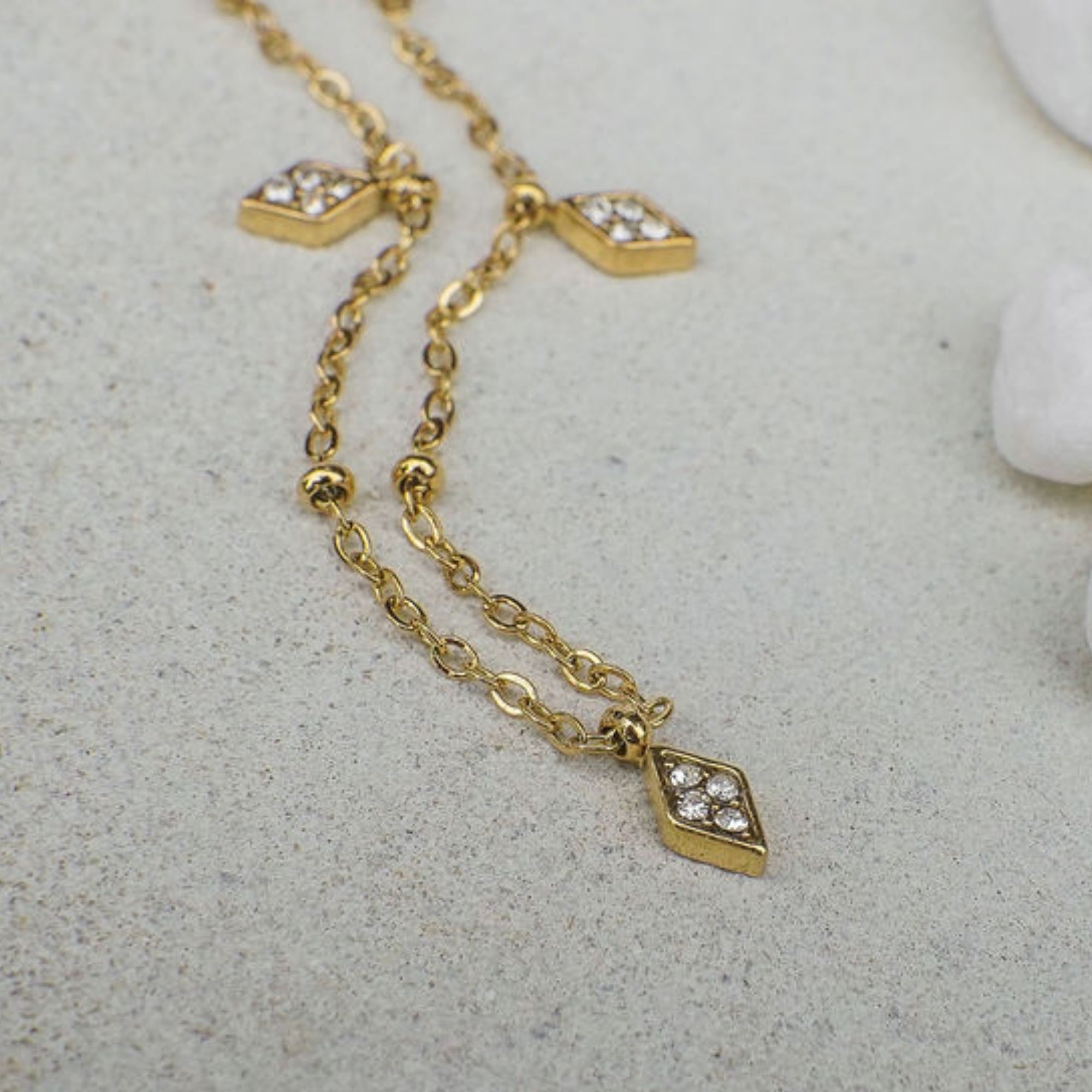 Gold necklace with diamond-shaped pendants on a light gray surface