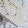 Gold necklace with pink gemstones on a white stone surface