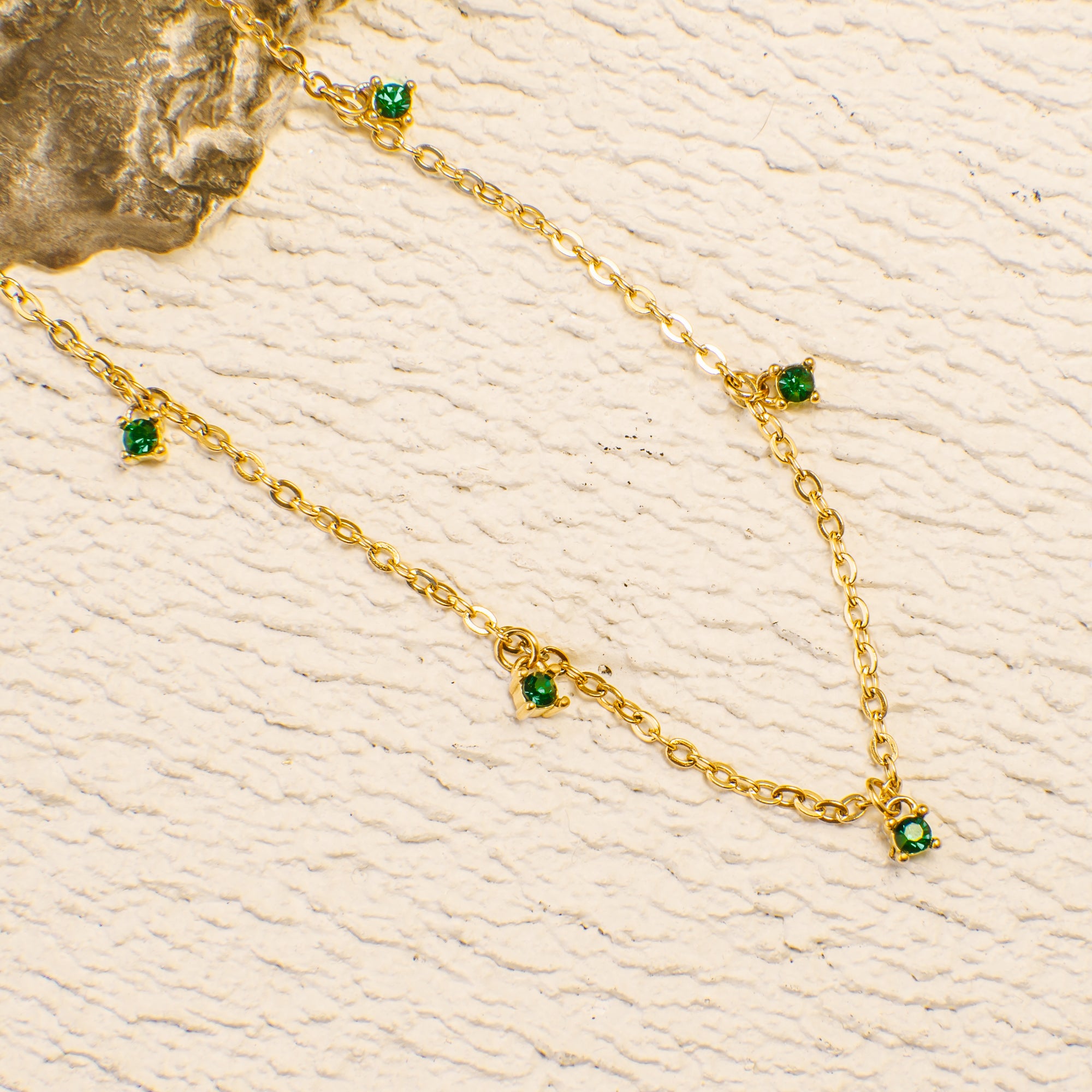 Gold necklace with green gemstones on a textured beige background