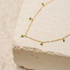 Gold necklace with green gemstones on a textured beige surface