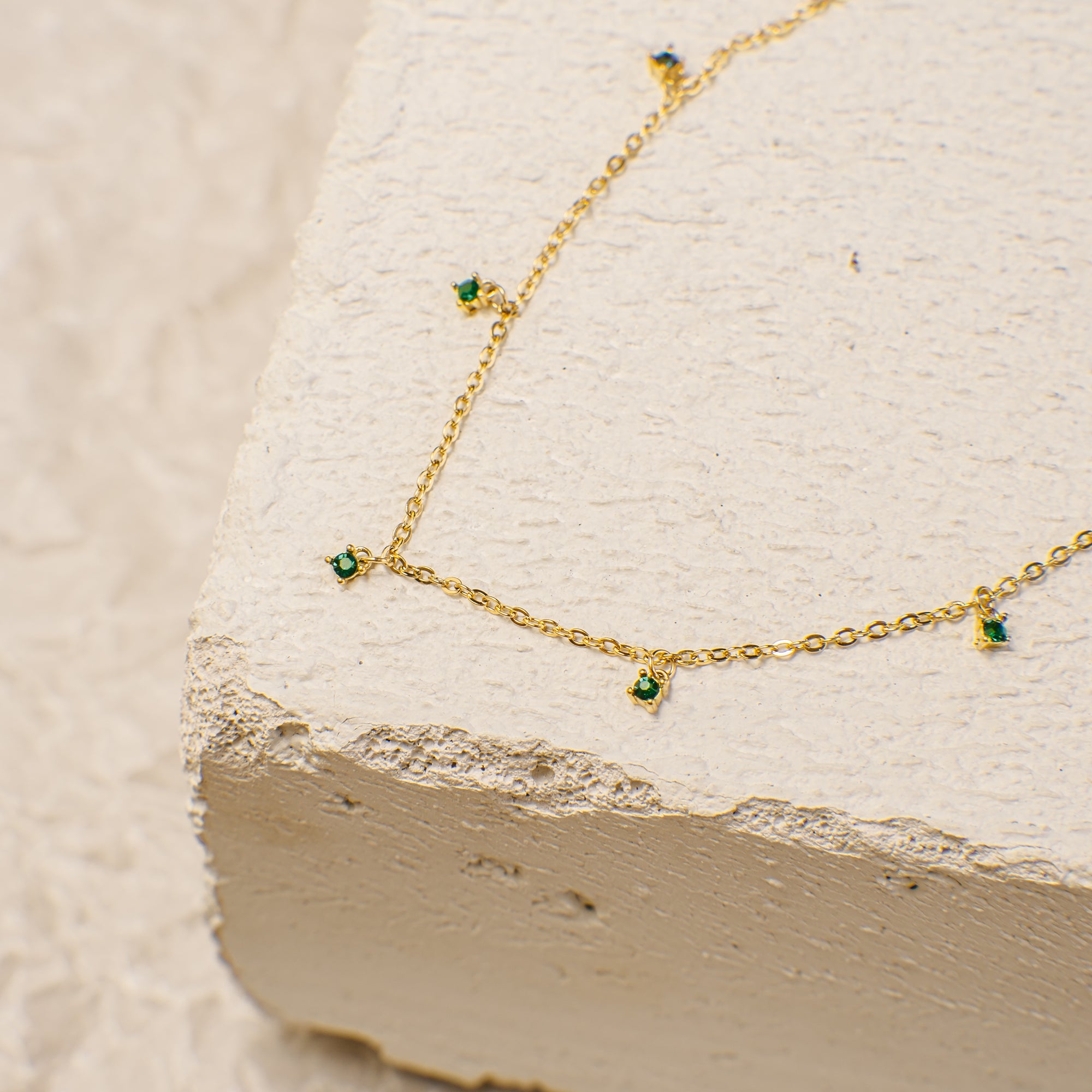 Gold necklace with green gemstones on a textured beige surface