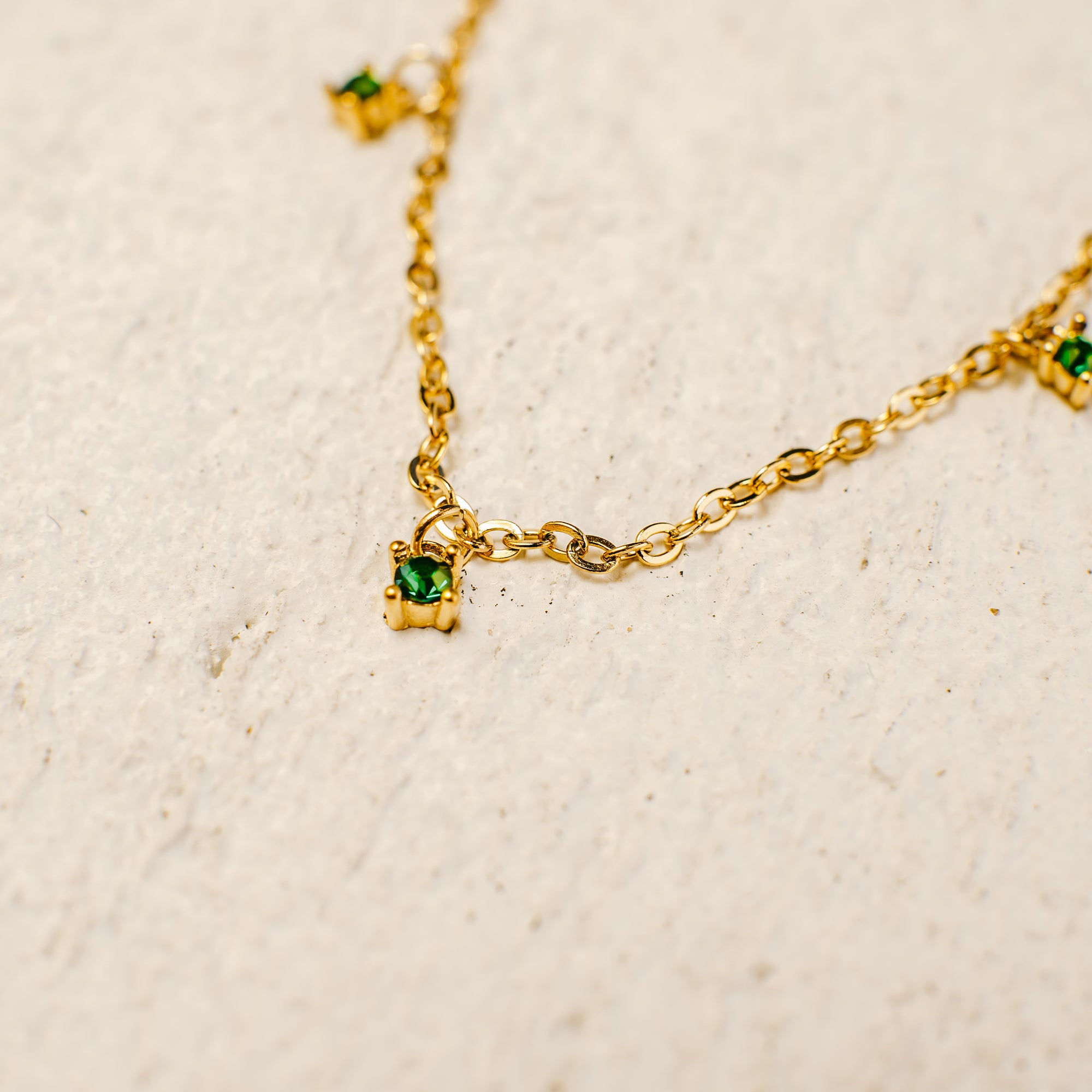 Gold necklace with green gemstones on a beige background