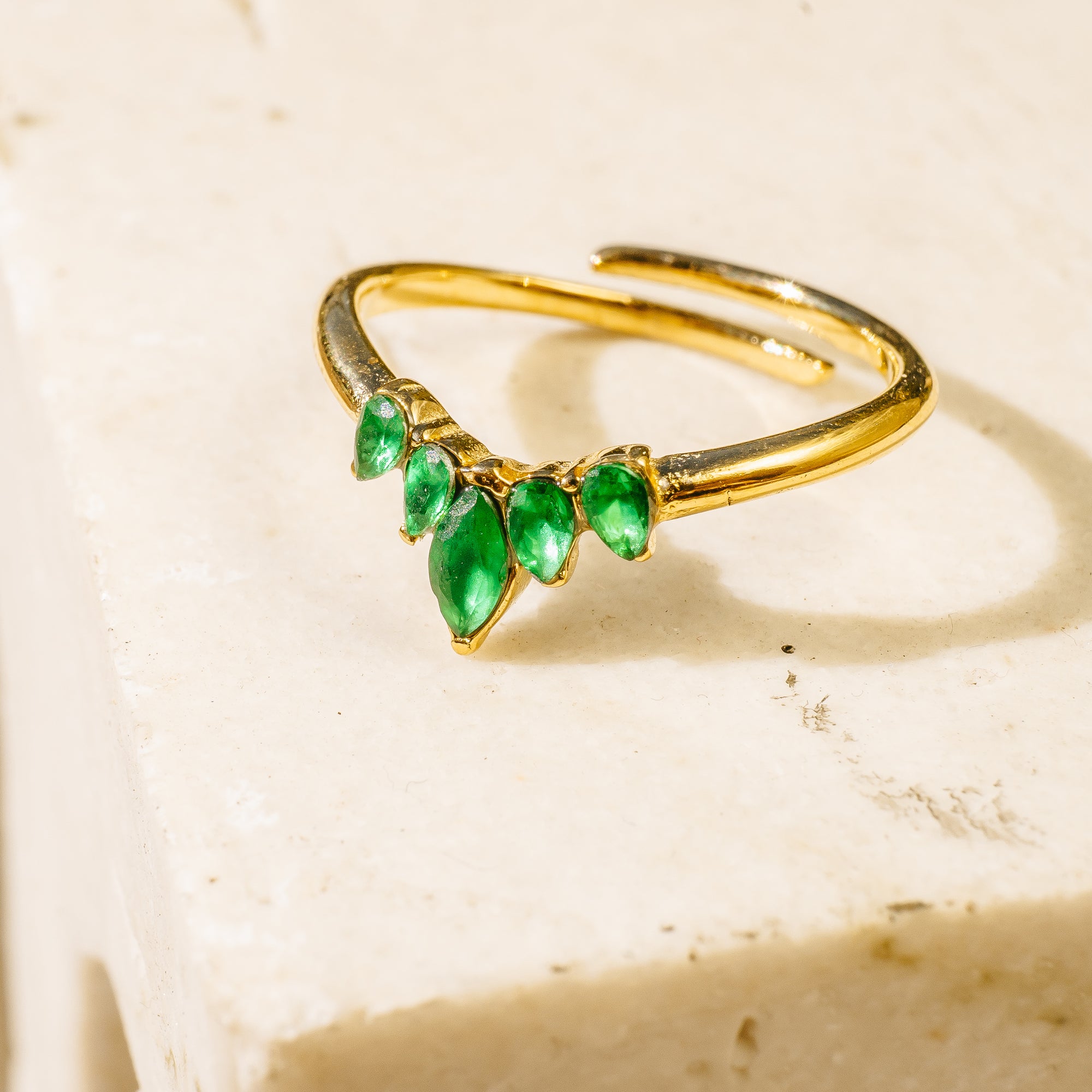 Gold bracelet with green gemstones on a beige background