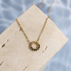 Gold necklace with green gemstones on a beige card against a water background
