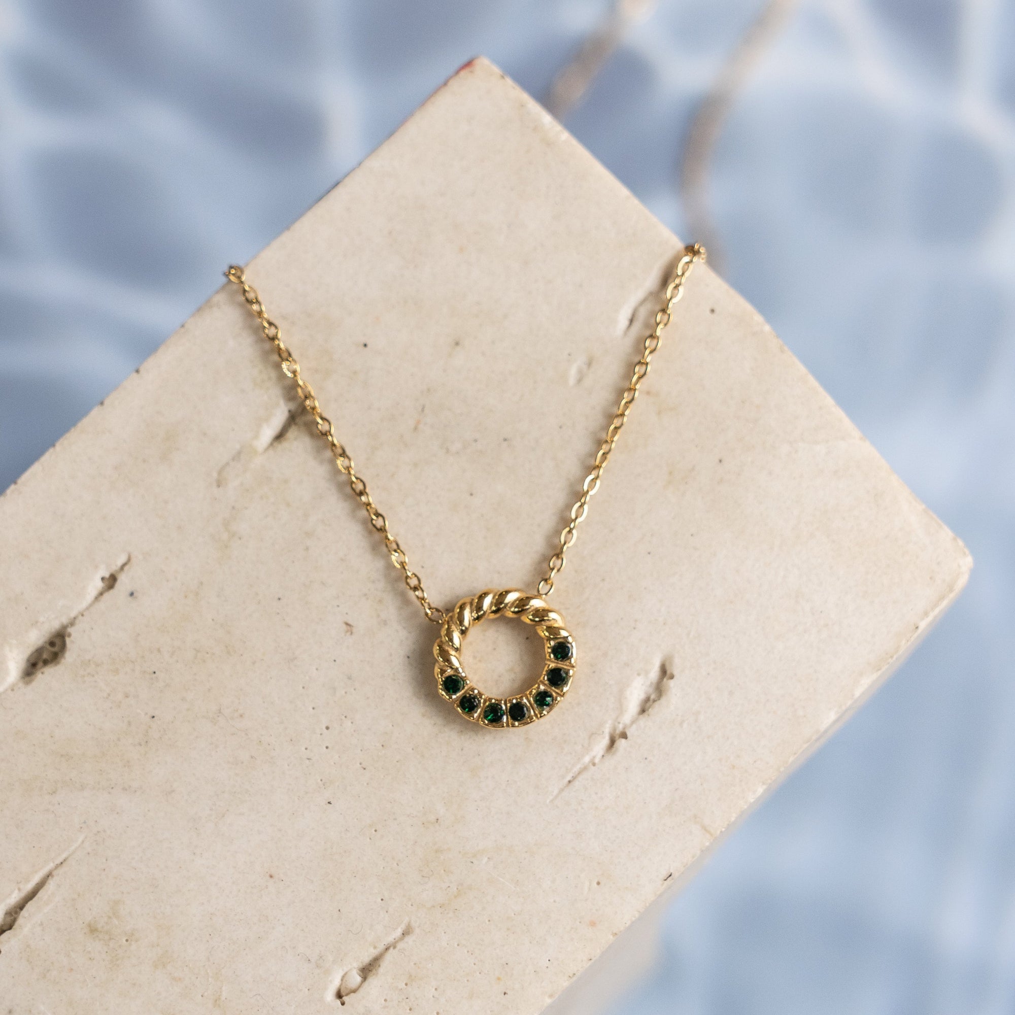 Gold necklace with green gemstones on a beige card against a water background