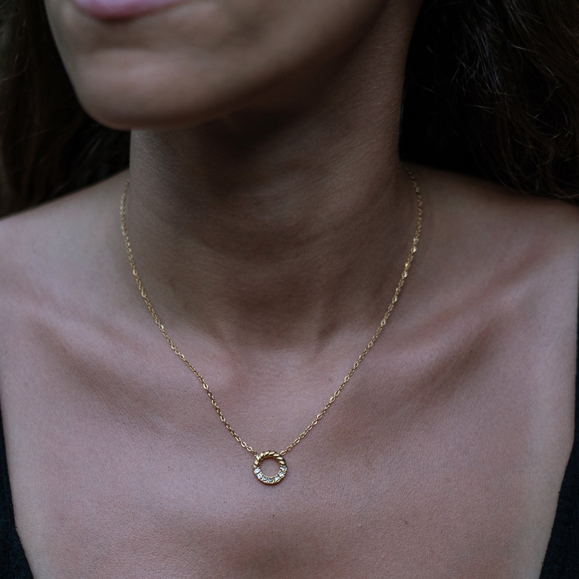 A model wearing a gold necklace with circular pendant and zirconia