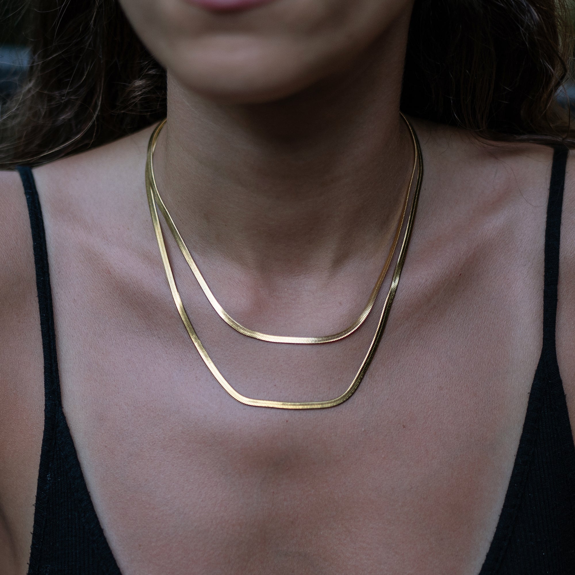 A model wearing two thick gold necklaces as stacked accessories