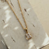 A rose quartz zirconia pendant necklace with a golden chain displayed on a textured surface.