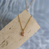 A rose quartz gold necklace on a beige wood surface