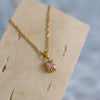 A rose quartz zirconia pendant necklace with a golden chain displayed on a beige card.