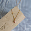 A rose quartz gold necklace on a beige wood surface