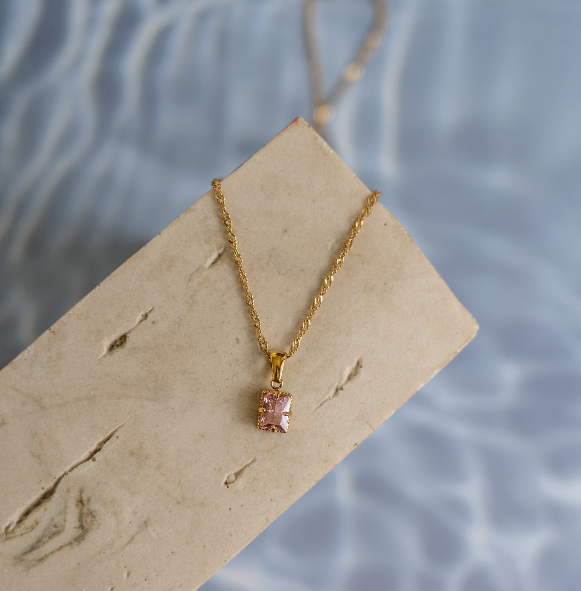 A rose quartz gold necklace on a beige wood surface