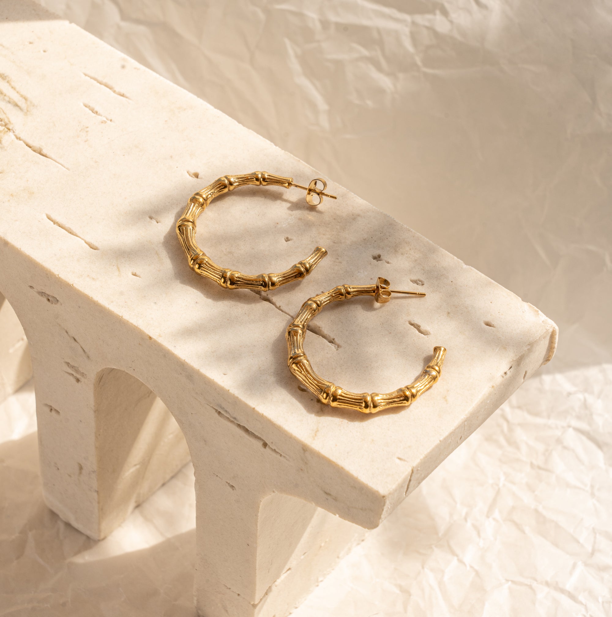 A pair of gold-colored hoop earrings placed on a white wooden surface with a textured background.
