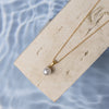 A single-strand pearl necklace with a gold clasp, displayed on a piece of neutral-colored fabric.