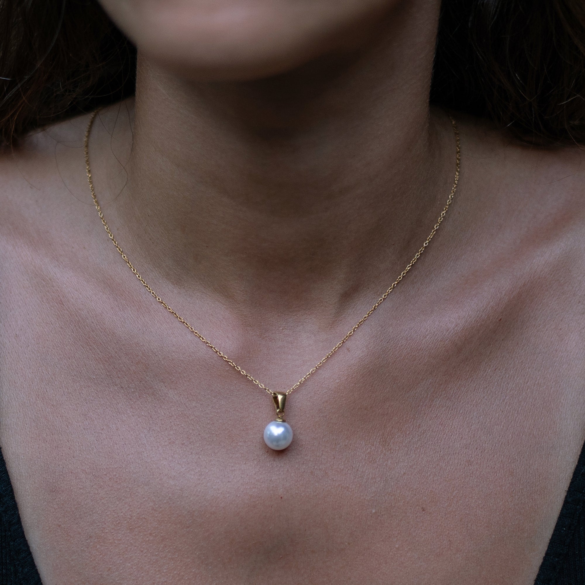 A model wearing a gold necklace with white pearl pendant