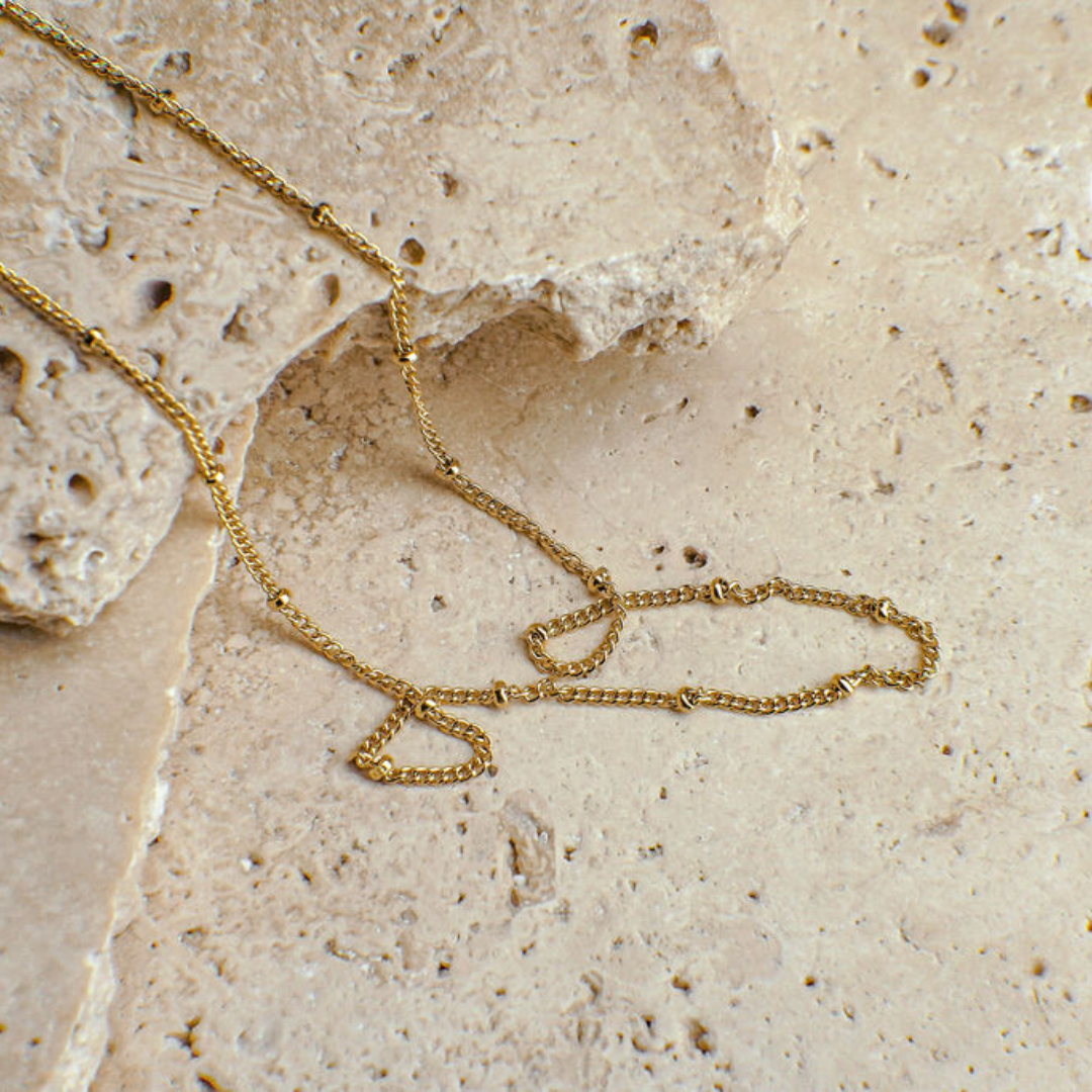 Gold chain necklace on a textured beige surface