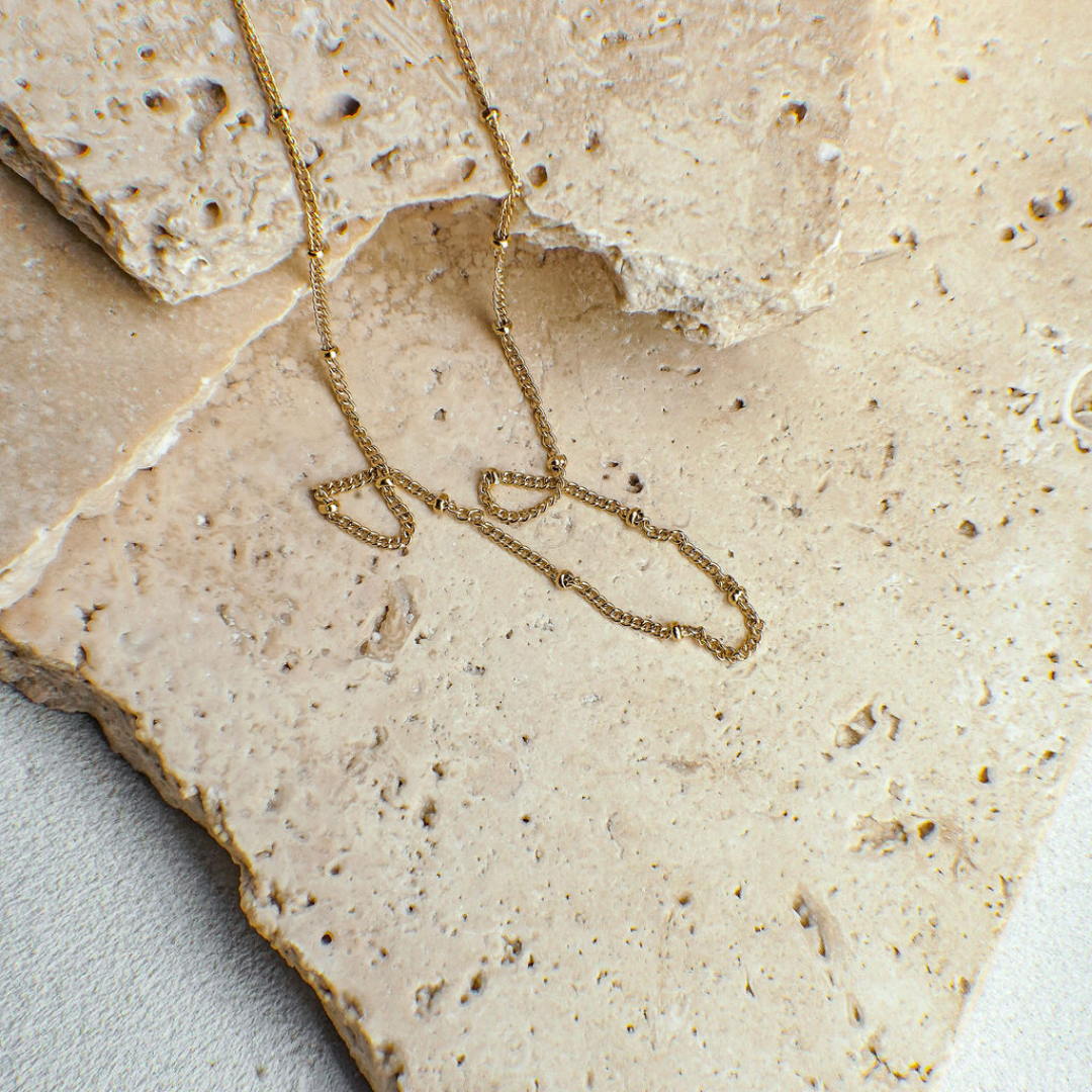 Gold necklace on a textured beige stone surface