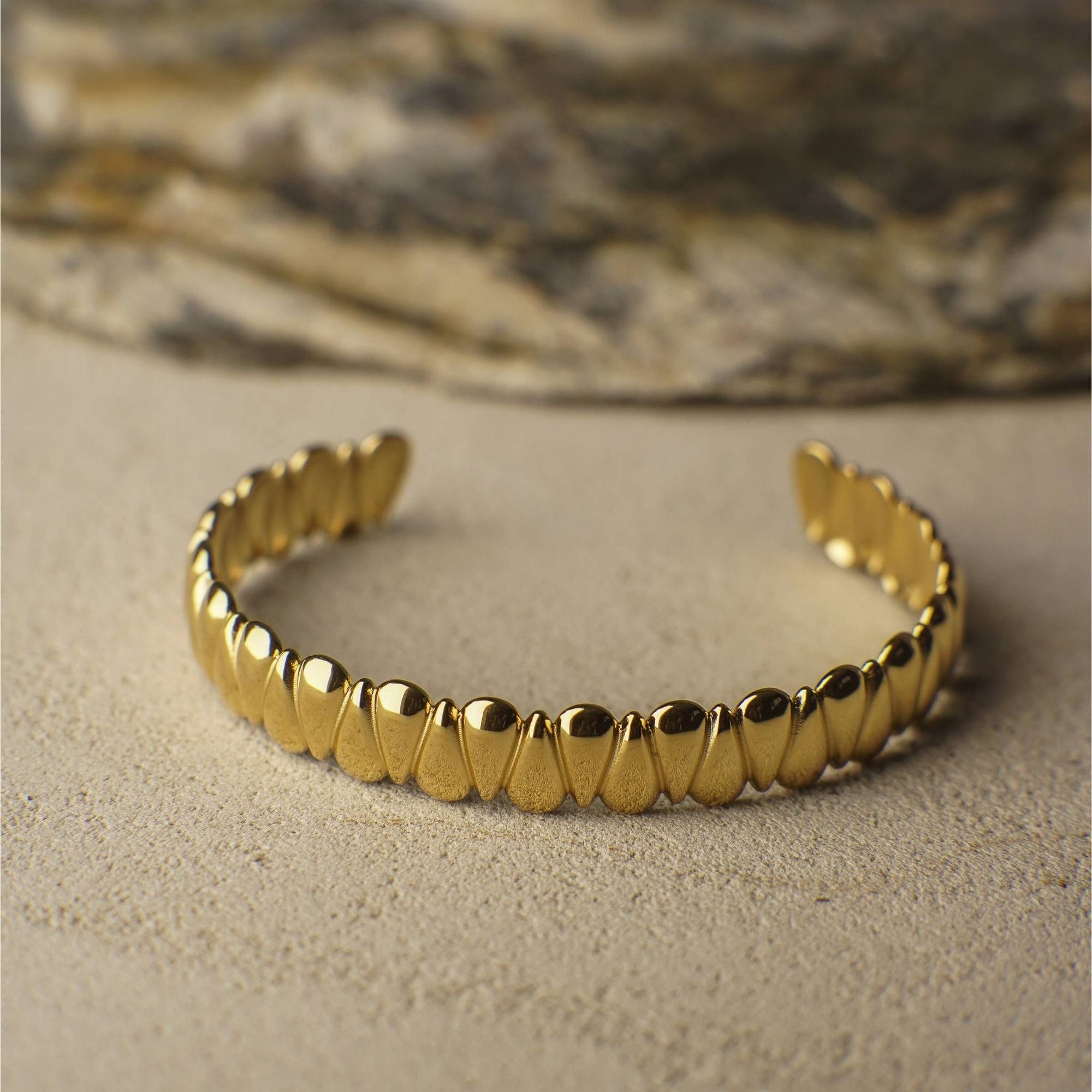 Gold bracelet on a textured beige surface with a blurred natural background