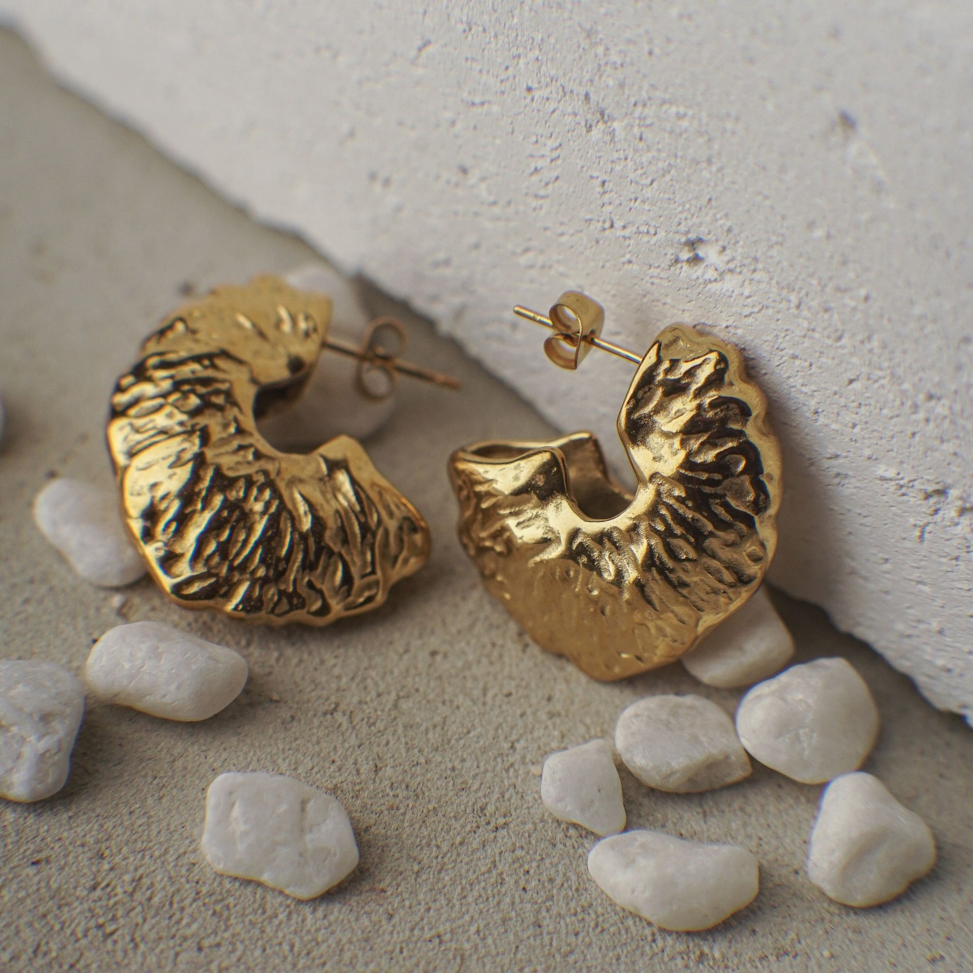 Gold hoop earrings on a textured surface with small stones