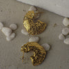 Gold textured earrings on a stone surface with small stones around