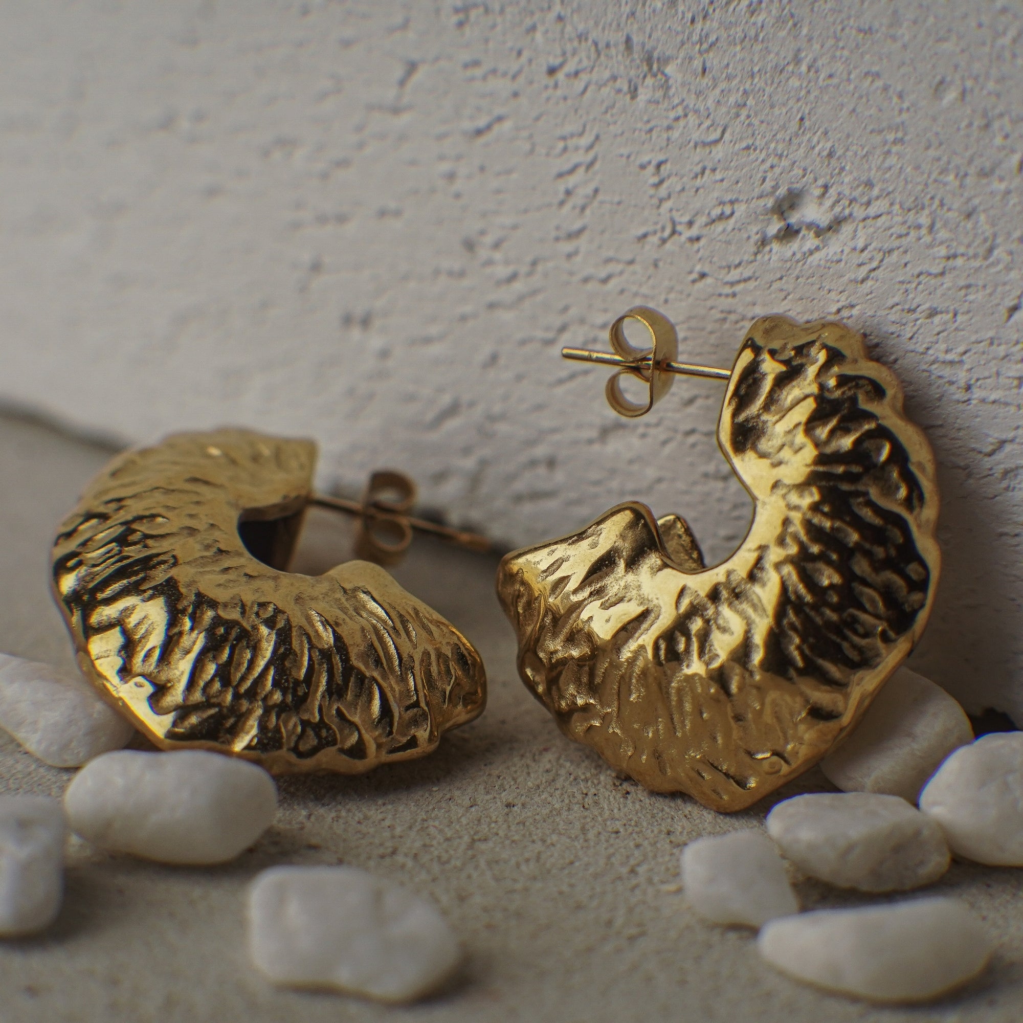 Gold hoop earrings on a textured surface with pebbles