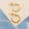 Gold hoop earrings on a textured beige surface with a blue gradient background