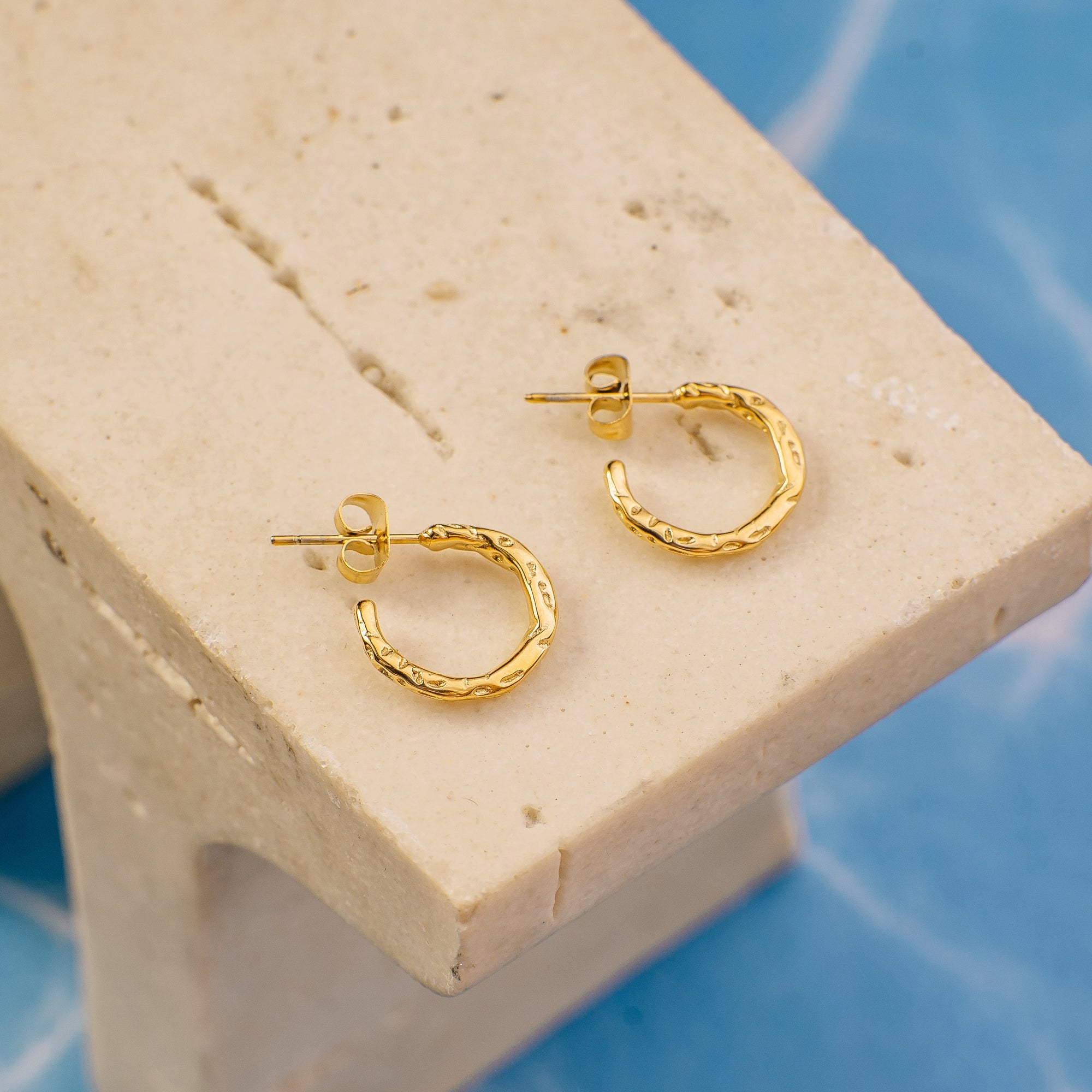 Gold hoop earrings on a beige stand with a blue textured background