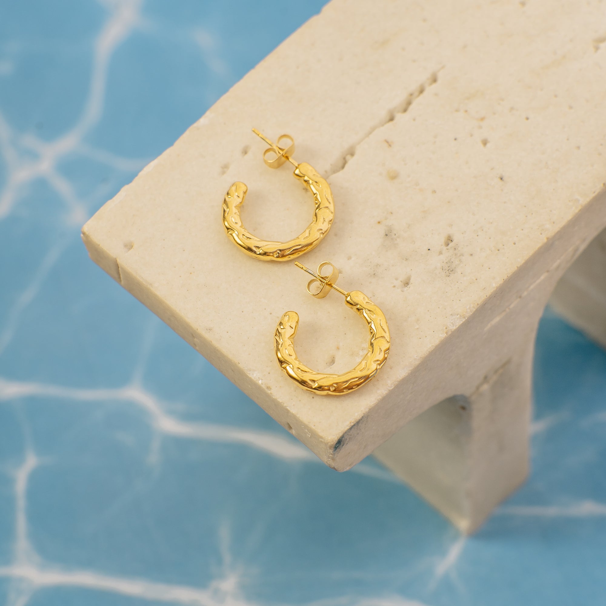 Gold hoop earrings on a beige stand with a blue textured background