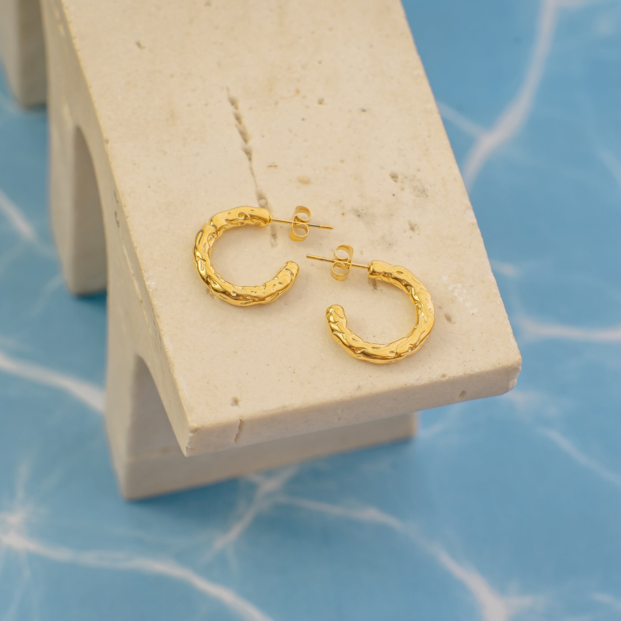 Gold hoop earrings on a beige stand with a blue background