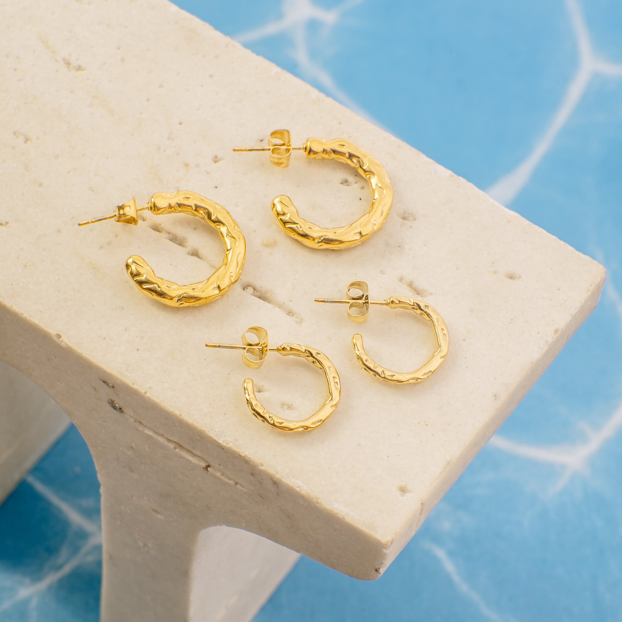 Gold hoop earrings on a white stand with a blue background