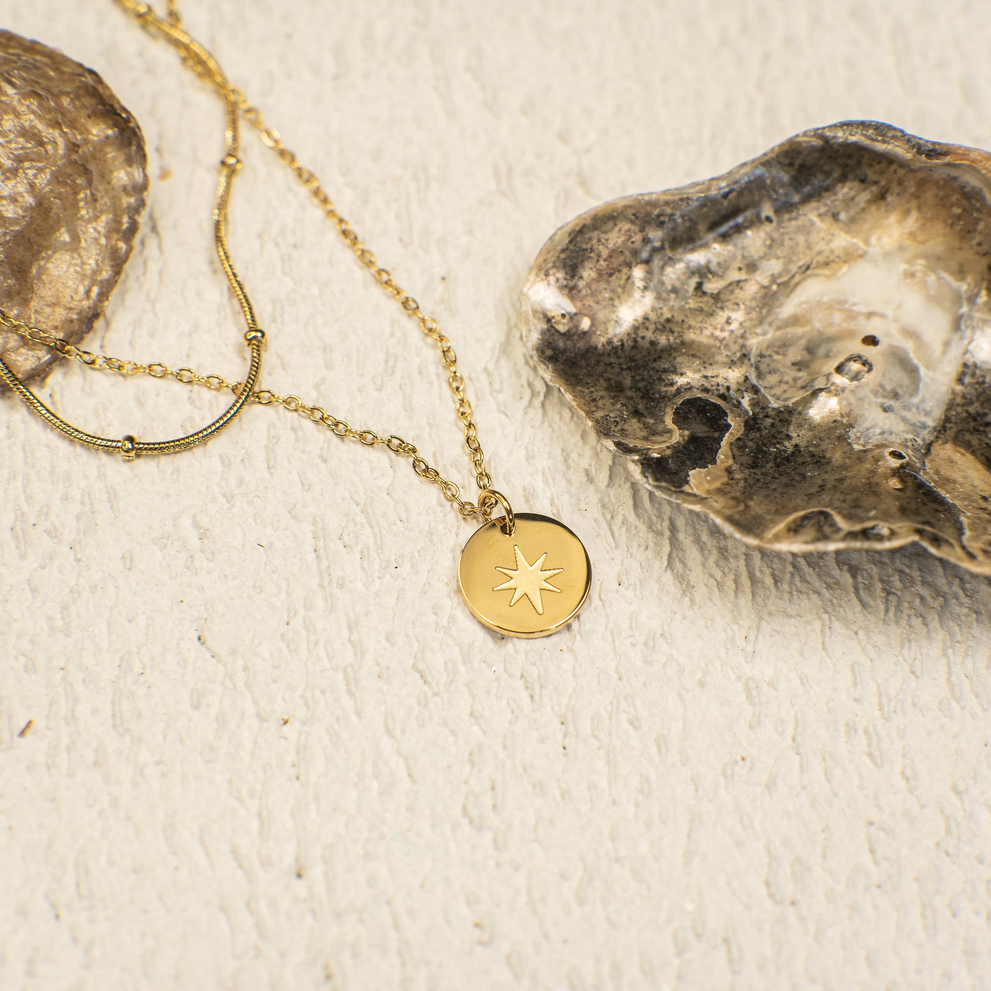 Gold necklace with a star pendant on a textured beige surface