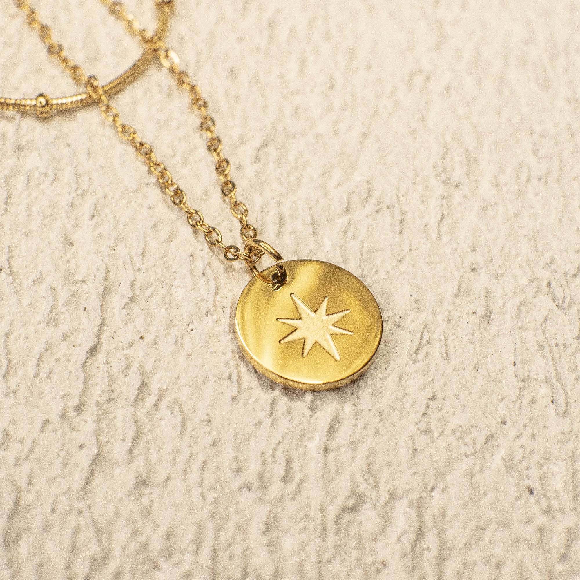 Gold necklace with a star pendant on a textured beige background